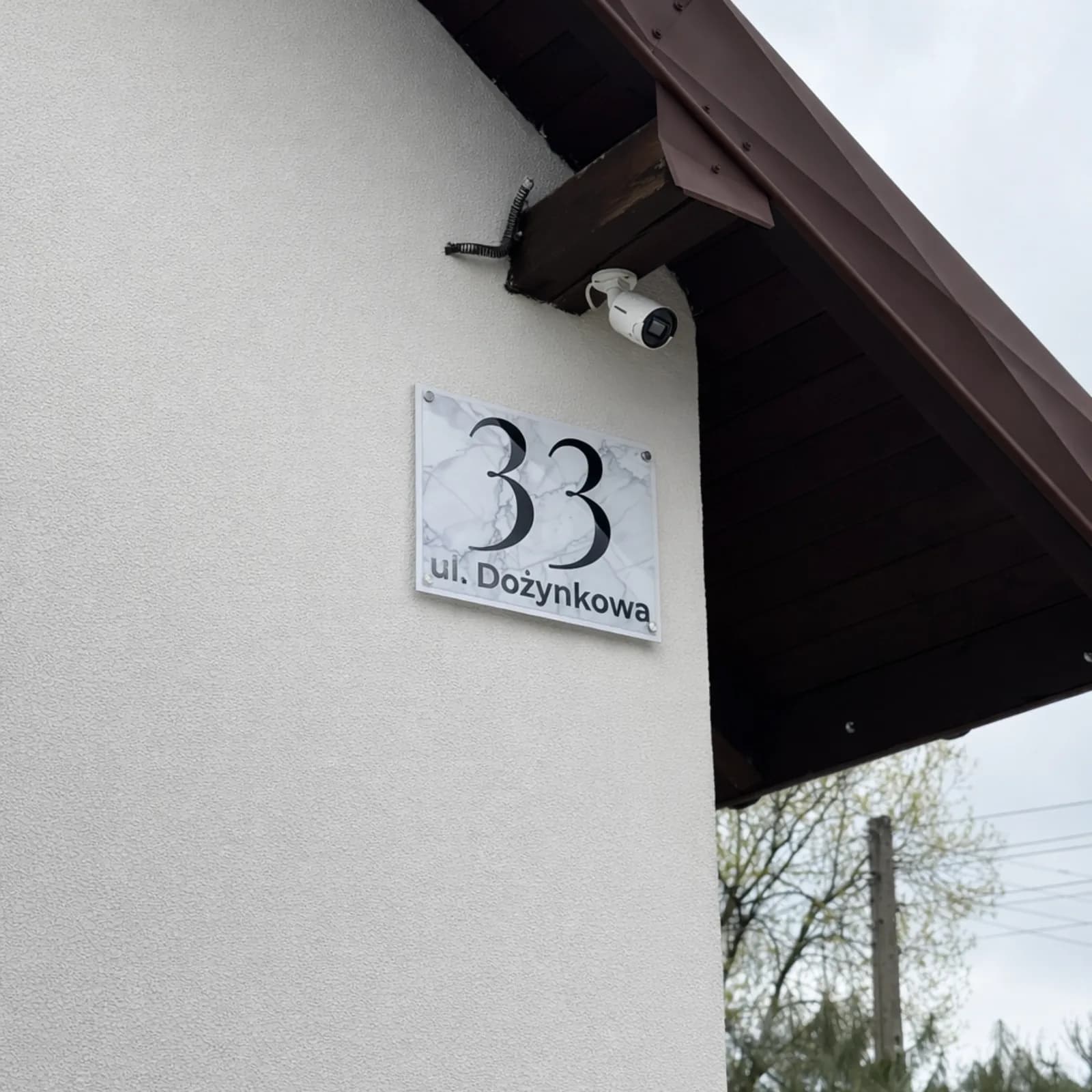 Glossy metal address sign with white marble-effect design, house number 33, mounted on a house facade outdoors — real product photo