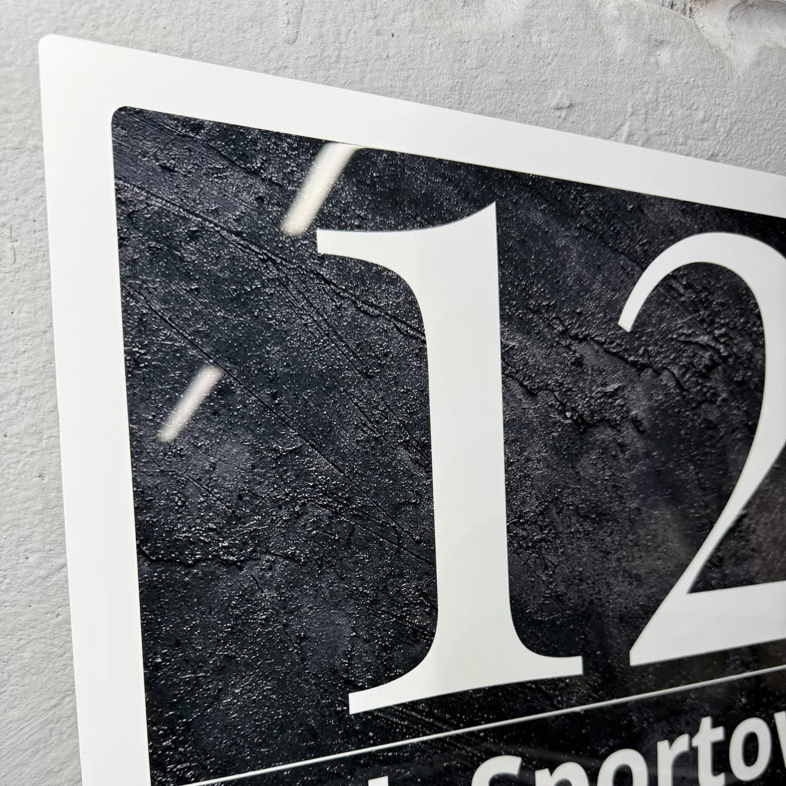 Macro detail of the anthracite-effect printed surface and crisp white numerals on a glossy metal address sign — real photo